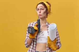 self-confident-female-builder-wearing-goggles-white-top-and-checkered-shirt-protective-gloves-holding-drill-and-papers-being-dirty-after-hard-work-isolated-over-yellow-wall-mainte.webp